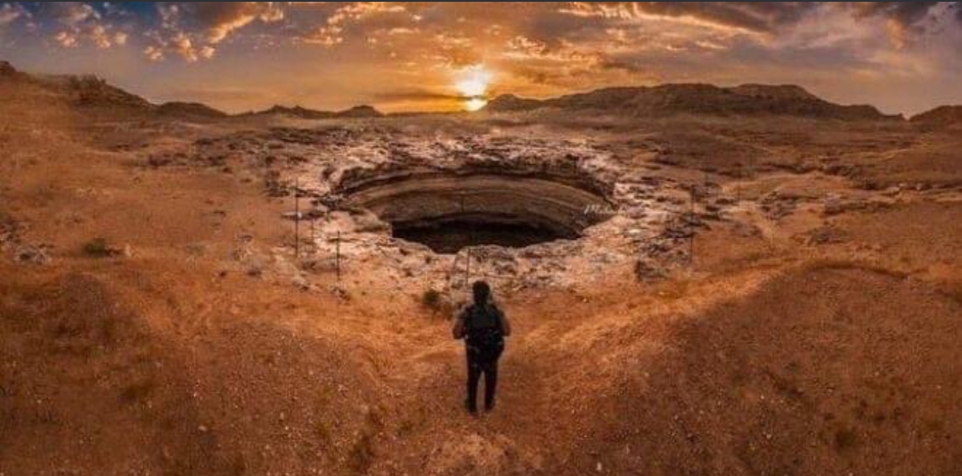 يحوم حول كل شئ غير مألوف الكثير من الحكايات العجيبة ومن ضمن هذه الأشياء الغريبة حفرة غامضة تتواجد في شرق اليمن أُطلق عليها العديد من المسميات منها "قعر الجحيم" ، "سجن الشياطين" ، "بئر برهوت" فما قصة هذه الحفرة؟! _ موقعها ووصفها تقع هذه الحفرة العملاقة في صحراء محافظة مهرة وهي أقرب إلي الحدود مع عمان من العاصمة صنعاء علب بعد 1300 كم بعرض 30 مترا ويبلغ عمق الحفرة حوالي112 مترا ، يبلغ عرضها عند السطح 30 مترا فيما يتوسع ليبلغ 116 مترا في أسفل الحفرة. _ بعض الأقاويل المتداولة عنها يقول الفولكلور المحلي أنها أُنشئت كسجن للشياطين وذلك لما يتصاعد منها من روائح كريهة وسامة. بينما اقترح كريس فوغويل أستاذ علم الجليد وعلم المناخ القديم بجامعة كيلي أن تلك الحفرة عبارة عن بينغو (تل علي شكل قبة يتكون من طبقة من التربة فوق نواة كبيرة من الجليد) منهارة. وأشار فوغويل مجددا اقتراحه بعد ذلك أن الحفرة لم تكن بينغو بل كانت ميزة أو حفرة ناتجة عن تآكل الحجر الجيري أو نقل الأملاح الجيولوجية أو المحاليل الملحية. ويُقال أن مياه ذلك البئر من أسوأ المياه علي هذا الكوكب. بينما أوضح صلاح بابير المدير العام لهيئة المسح الجيولوجي والموارد المعدنية في مهرة أن الحفر عميقة للغاية ويوجد القليل من الأكسجين بها مشيرا إلي عندما دخلوا البئر لاحظوا أشياء وروائح غريبة بالداخل. يتكهن البعض بأن البئر عبارة عن بركان هائل وسينفجر في النهاية بالإضافة إلي بعض الخرافات المحلية والتي تشير إلي أنه يمكن امتصاص الأشياء القريبة من الحفرة تجاهها. ماذا وجد المستكشفون بها؟! استكشفها فريق عُماني "أول من نزل إلي تلك الحفرة" في إطار تعاون مشترك مع هيئة يمنية متخصصة استخدم فيها الفريق معدات تسلق حديثة وطائرة مسيرة وجديرا بالذكر أنهم أخذوا صورا لكل شئ مميز بها لكن أكثر ماوجوده مميزا هو وجود أنواع جميلة جدا من اللآلئ تُعرف ب"لؤلؤ الكهف" ، كما وثق الفريق وجود حيوانات مختلفة داخل الحفرة مثل "الزواحف ، الأفاعي ، الضفادع، النمل ، الخنافس ، الطيور". بالإضافة إلي إنبثاق المياة من الجوانب لتكون شلالات بديعة ووجود مجموعة متنوعة من الترسبات الكهفية. فائدتها صرح د. محمد بن هلال الكندي جيولوجي ورئيس مركز استشارات علوم الأرض أنه يمكن تطوير الحفرة كمنطقة سياحية كما تمثل أرشيفا طبيعيا لكثير من البيانات العلمية منها(تغيرات المناخ خلال آلاف السنوات). لكن مايزال العديد من السكان المحليين غير مرتاحين لزيارة الحفرة الواسعة أو حتي التحدث عنها.